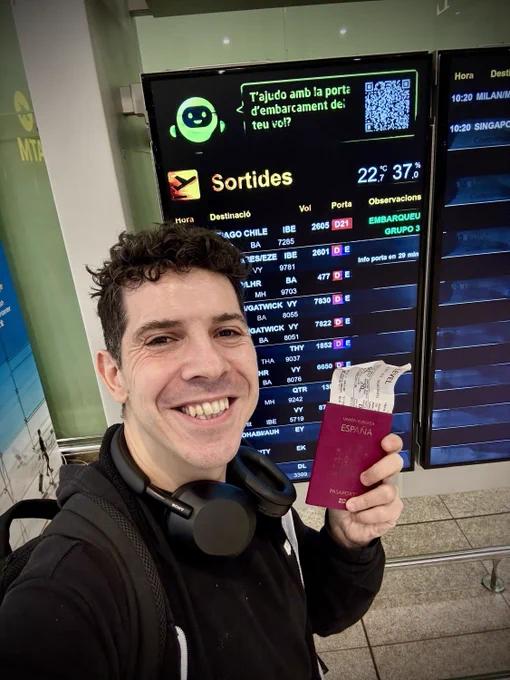 Sosteniendo mi pasaporte con un monitor del aeropuerto de Barcelona, detrás que aparece el vuelo a Santiago de Chile