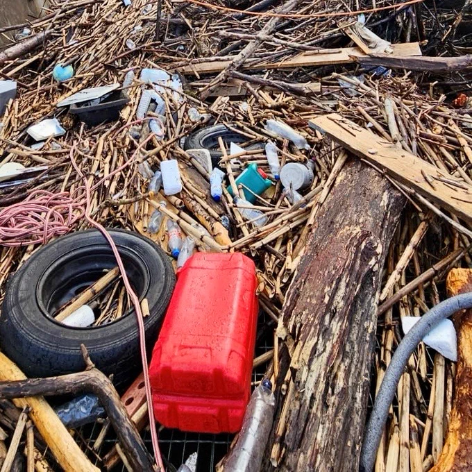 River debris including branches, a car tyre, and assorted plastic containers.