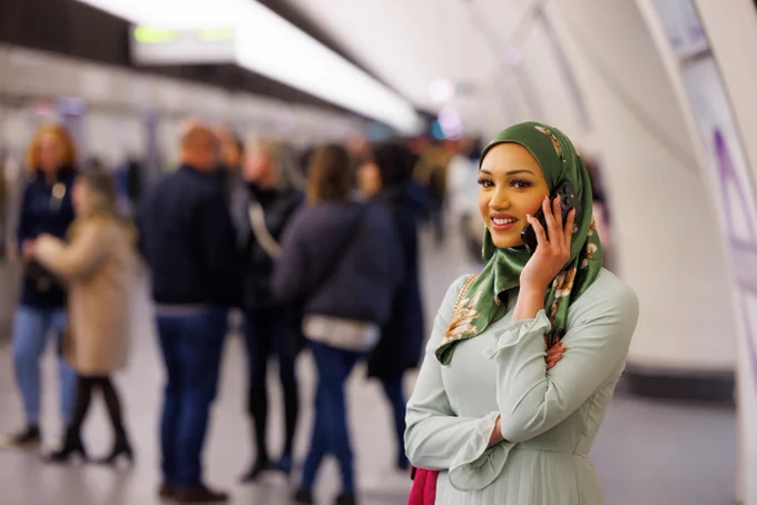 A woman smiles as she presses her mobile phone to her ear, standing on the platform. 