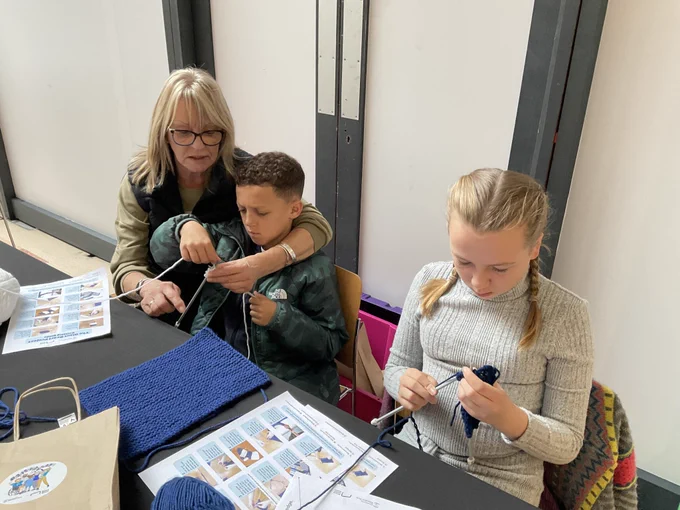 A photo of two young people and an adult knitting