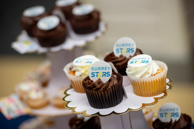The image shows chocolate and vanilla cupcakes displayed on a cake stand. They have Surrey STARS logos on top of them. 