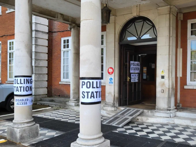 Entry way into a hall wit two pillars and a tiled landing. Two white posters taped onto the pillars with text reading 'polling station'