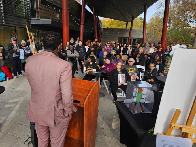 Photograph of the Public Advocate from behind. He speaks from a podium as members of Families for Safe Streets and others listen