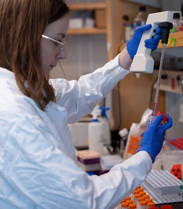 PhD candidate Kate Donald, pictured from the side, holds a large test tube in one hand and a pipette in the other, transferring a red liquid into the tube.