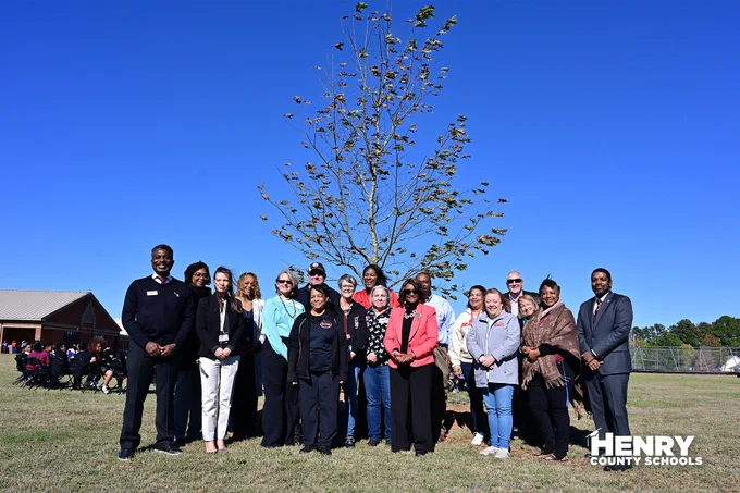 School leadership and teachers of past and present in front of newly planted tree.