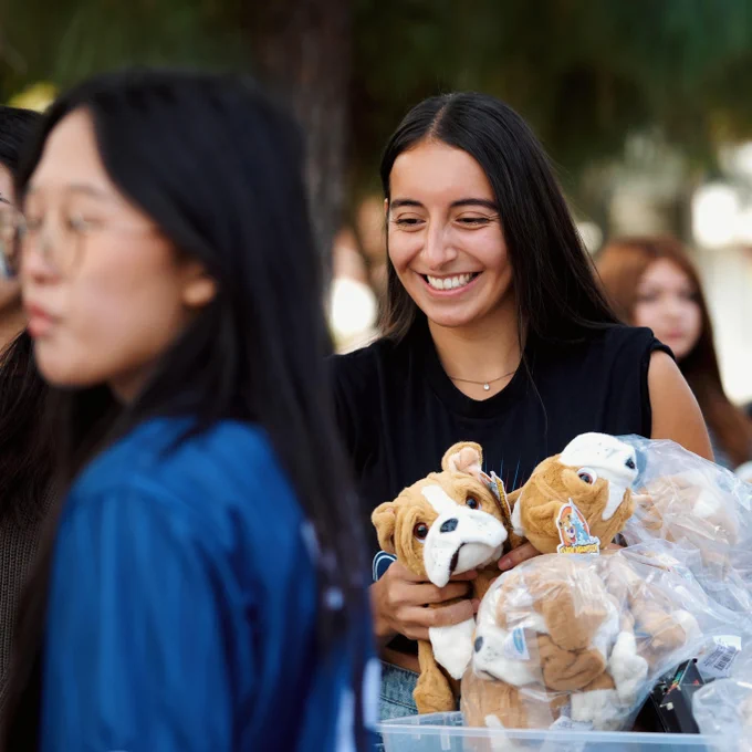 Person smiling while holding stuffed animal toys at an outdoor event.