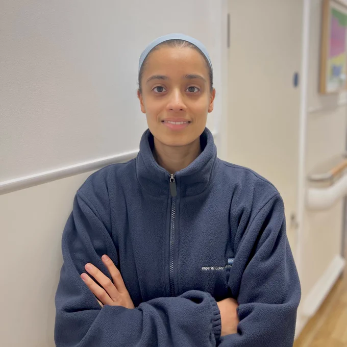 Close up photo of a support worker at Imperial College Healthcare. They are wearing a blue NHS fleece and cap and smiling towards the camera.