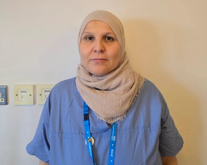 Close up photo of a support worker at Imperial College Healthcare. They are wearing a blue NHS uniform and beige hijab and smiling towards the camera.