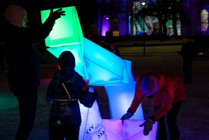 Two adults and a child are twisting a particularly large sculpture, working together by holding different parts of it while moving it into shape.
