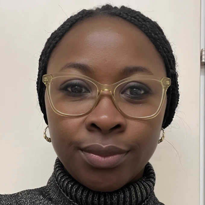 Close up photo of a support worker at Imperial College Healthcare. They are wearing a grey turtleneck jumper and smiling towards the camera.