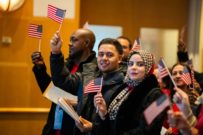 Group of individuals proudly waving American flags at a citizenship ceremony at the JFK Presidential Library.