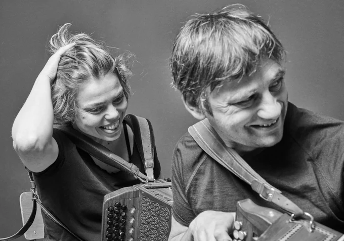 Black and white photo of Andy and Anne, who are sat holding their accordions and smiling. 