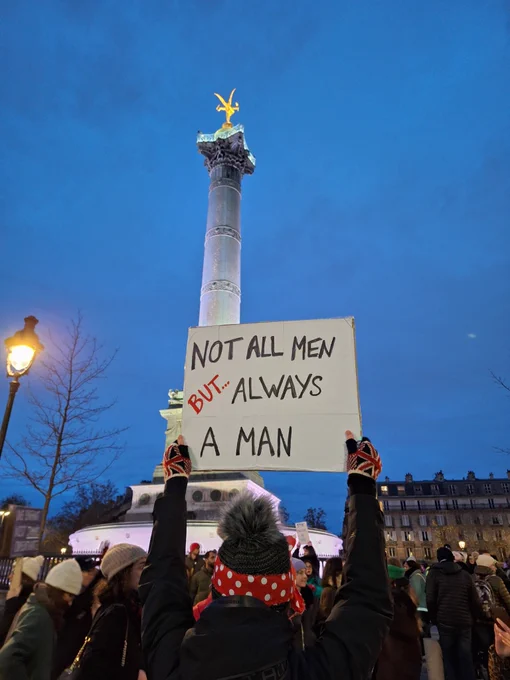 Manif NousToutes. Pancarte NOT ALL MEN BUT ALWAYS A MAN brandie face au Génie de la Bastille 