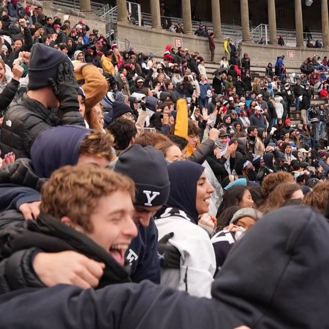 Crowd of excited spectators at a Yale University sports event, with some attendees wearing Yale apparel.