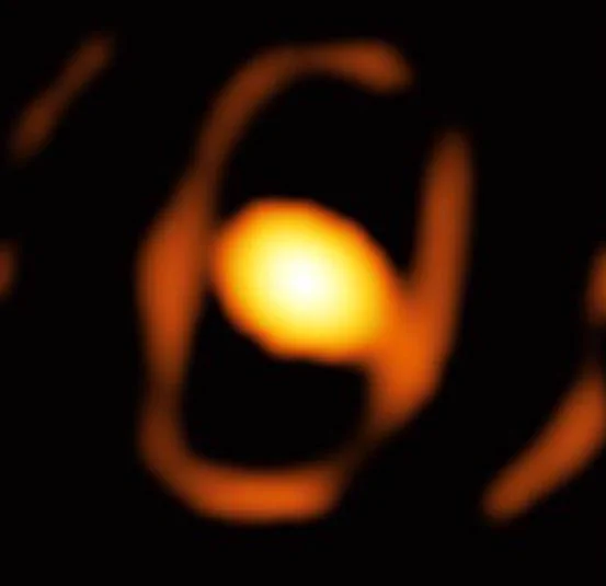 A blurry image of a dying star that appears as an orange circle with an orange egg-shaped cocoon surrounding it.