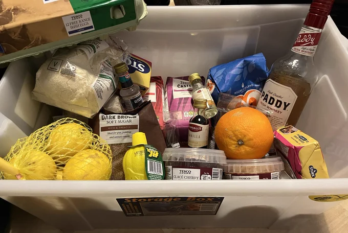 Whit plastic box containing packets of flour, sugars, ground almonds, and various other cake ingredients.
