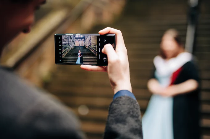 Colour photo of someone taking a photo of a graduating student stood at the stone steps in the New College Quad