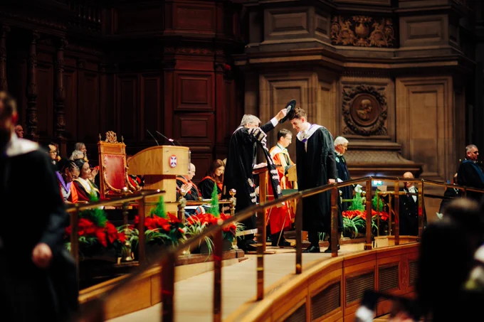 Colour photo of a graduating student getting tapped on the head by the graduation cap on the stage during the ceremony in McEwan Hall