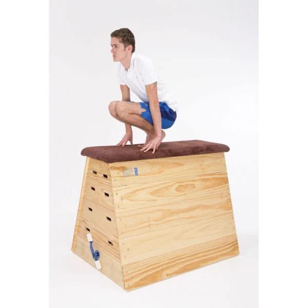 Student in a PE kit in a squat on position on top of a wooden gymnastics vault.