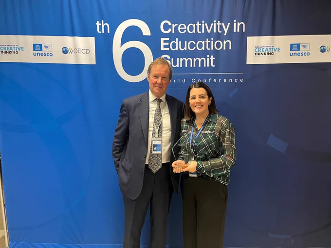Image of a man and woman standing up in front of a blue background. The woman is holding a glass award in her hands. 