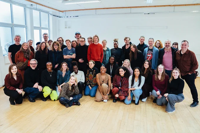 A photo showing a group of performers assembled in a rehearsal room huddle