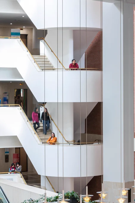A view of the spiral staircase at the British Library, with two visitors standing on the platform looking out at the space below.