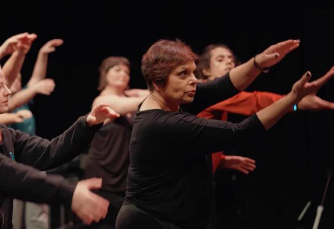 A group of dancers in black and red performing in a dark space.