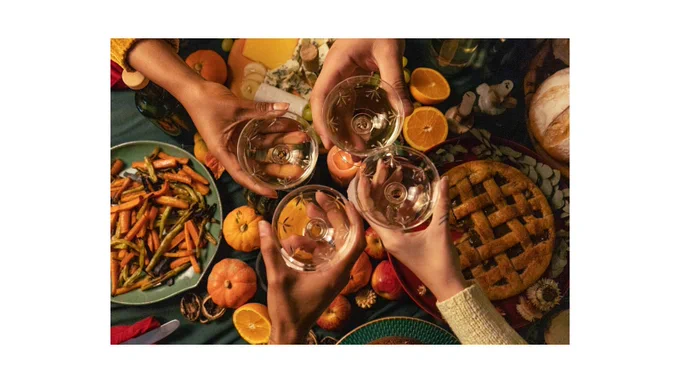 Variety of food on table with four people holding drink glasses together