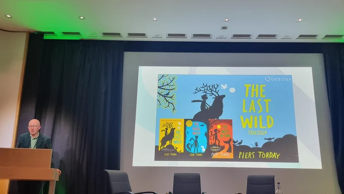 Piers on stage, with the book covers for The Last Wild trilogy on the slide next to him.