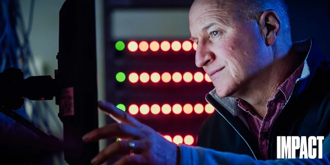 IMAGE: Portrait of Dr. Jeff Dahn looking at a screen. Small red lights in the background. Small white text in bottom right corner ”Impact”.