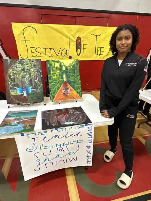 Student stands next to table showcasing Paintings in Lincoln High Practice Gym