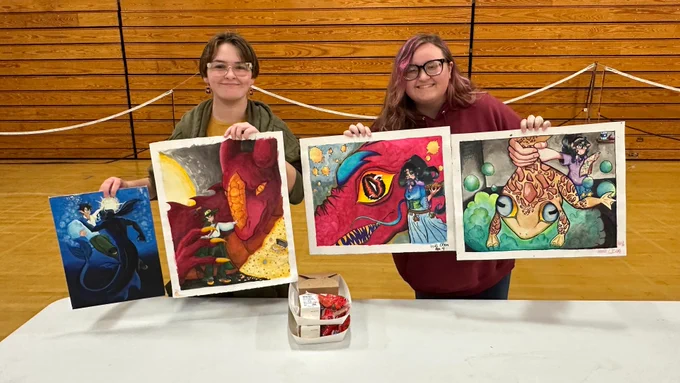 Two students hold two paintings each in Lincoln High Practice Gym
