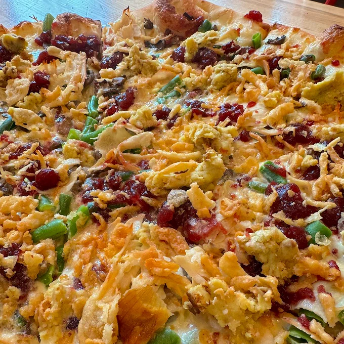 close up shot of the Thanksgiving pizza with creme mushroom base, mozzarella, button mushrooms, green beans, cranberry sauce, turkey, and fried onions.