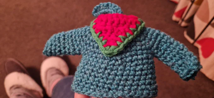 The back of a tiny crocheted jumper including a Green and Red neckerchief