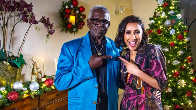 Anita Rani and Rudolph Walker stand together in front of a Christmas tree