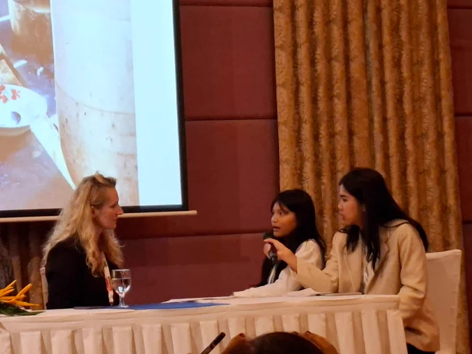 14 year-old Srey is sitting on the stage of a conference room, telling her story to the moderator of the event. (c)HI