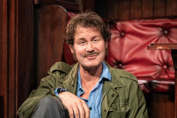 A photo showing a man in vintage gear on a wood-panelled stage, looking into the camera 