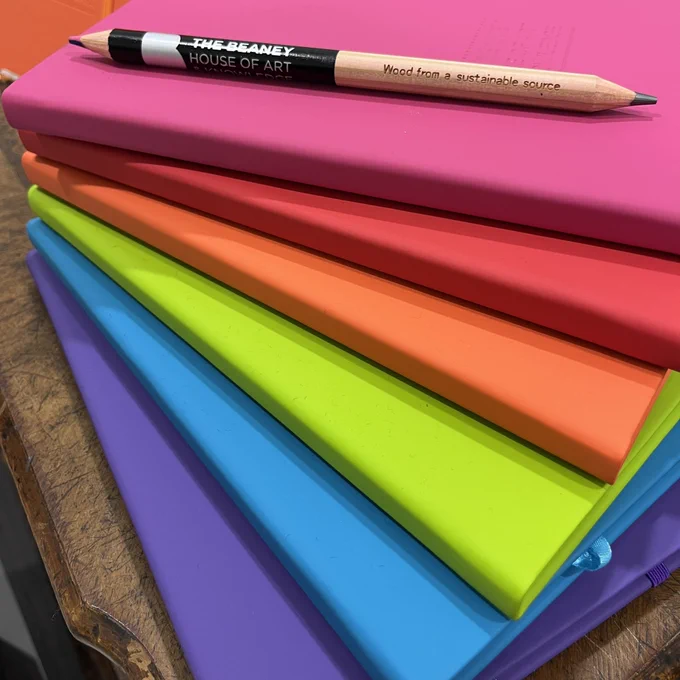 a range of colourful notebooks in orange, red, green, purple, pink and blue. Each is debossed with The Beaney logo