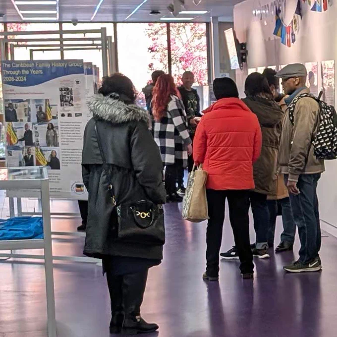 A group of people standing in a gallery chatting and looking at an exhibition about Caribbean family history