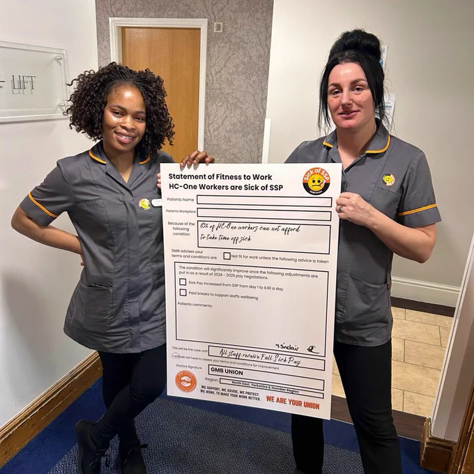 Two women in HC-One uniforms hold up a novelty size “sick note” calling for improved sick pay and paid breaks.