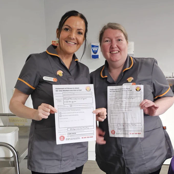 Two smiling care workers in uniform hold up sick note campaign props, which call for improved sick pay and paid breaks for care workers.