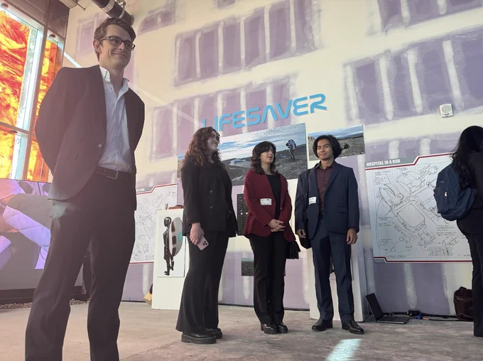 The team stands near posters showing industrial design sketches of the concept.