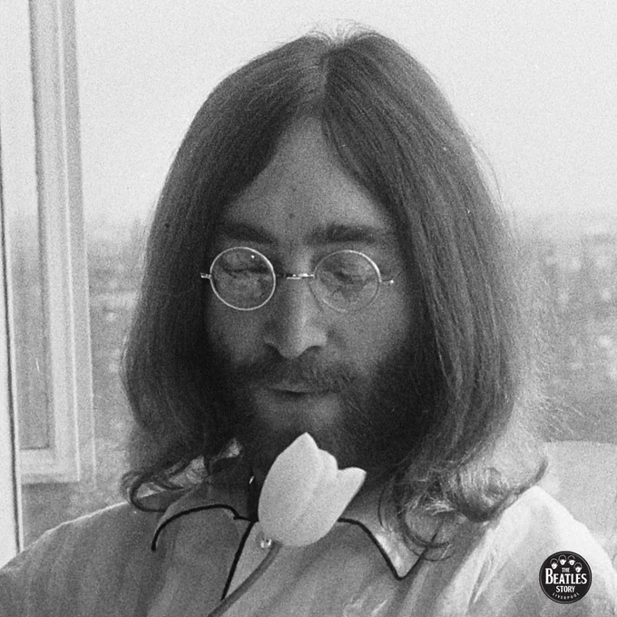 a black and white photo of john lennon during his bed-in with yoko ono in amsterdam. he is holding a white tulip.