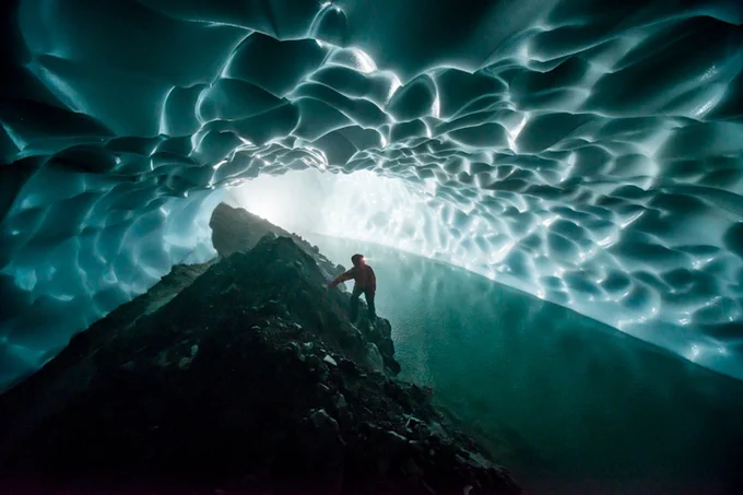 Dr. Penny Boston standing on a rock formation inside inside a glacier cave that looks like a tube of frozen, rippled water tubing around her. Credit: NatGeo, Carsten Peters