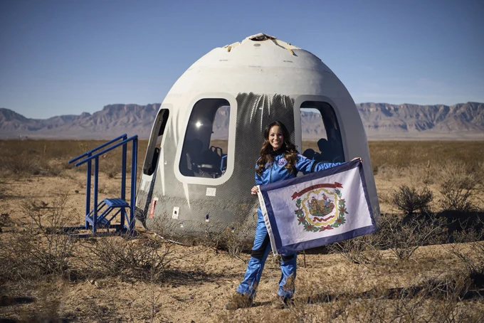 Emily holding a West Virginia flag in front of the landed Blue Origin capsule