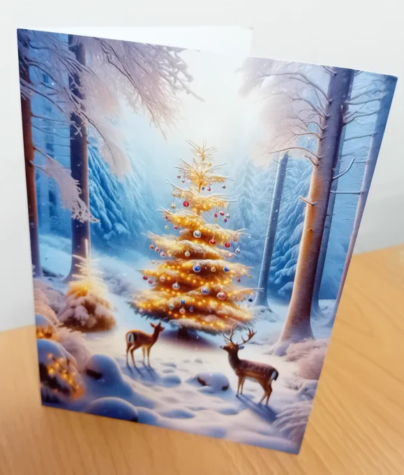 Card featuring a festive scene of two deer gazing at a snow covered and decoration adorned Christmas tree.