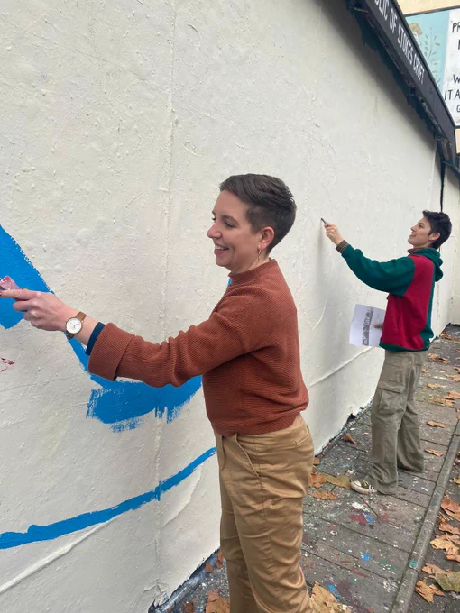 Carla painting some blue onto the whitewashed mural wall, the first layer of paint