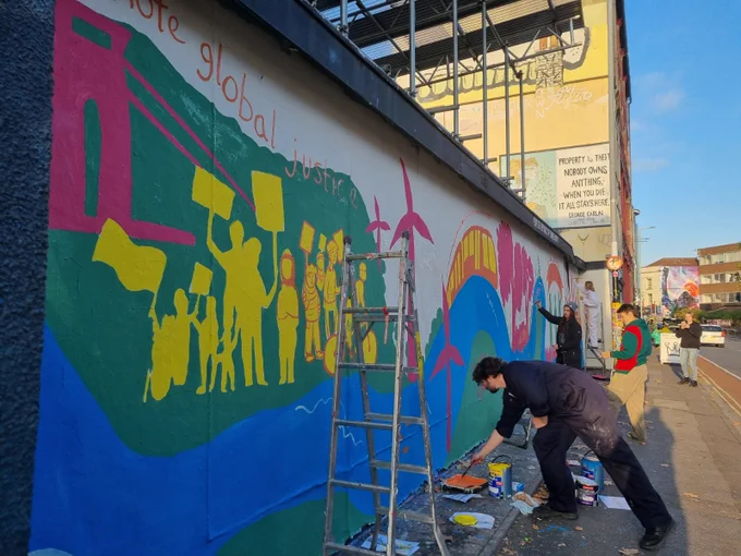 The mural is more than half done. Three people are working on different sections in different colours