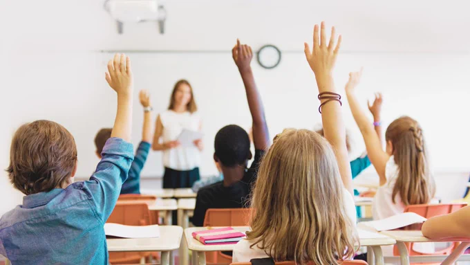A group of students raise their hands in a classroom. 