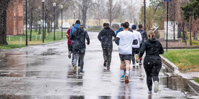 Cadets run down a paved street on a dreary day with rain and snow.